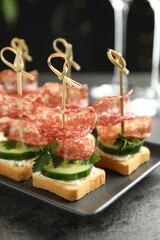 Tasty canapes with salami, cucumber and cream cheese on grey table, closeup
