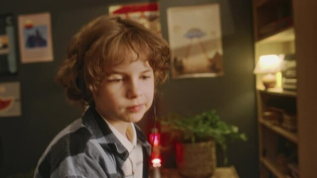 Tilt closeup of Caucasian boy with wired headphones turning on music on retro MP3 player and dancing weirdly alone at home