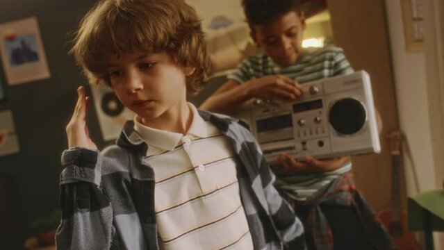 Pull out handheld footage of Black boy playing music on jambox and his Caucasian friend performing robot dance, friends hanging out at home after school, 90s atmosphere
