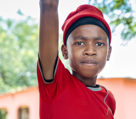 village african teenager boy , wearing a red beanie , standing in front of the house in the yard...