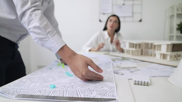 Skilled caucasian interior designer working with house model while discussing with asian architect engineer about house plan on meeting table with blueprint and house model scatter around. Immaculate.