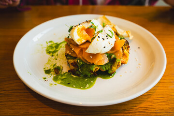 Potato waffle with salmon, poached egg in spinach sauce on white plate.