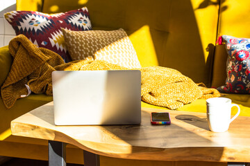 Modern interior in a Scandinavian style. Yellow sofa, laptop and tea cup on wooden table. A house from inside with stylish designer elements. Multicolored decorative pillows in Scandinavian style. 