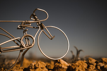 A miniature metal bicycle against a dark grey blue sky. Toy fake souvenir hand made craft mini bike...