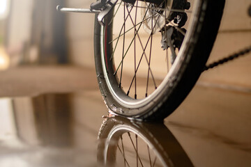 close up of rear bicycle wheel which is flat and parked on wet floor of house garage.