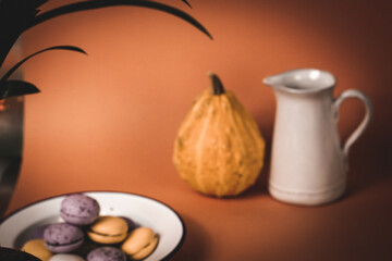 A plate with pumpkin-flavored macaroons. Cooked homemade cookies with rustic recipe. Pastry based on meringue from almond flour. Orange pumpkin in a background. Thanksgiving day table. Vintage photo