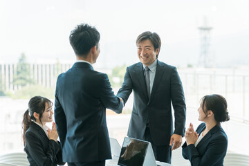 企業のオフィス・会議室で握手をして契約を結ぶビジネスマン
