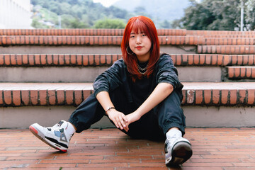 A casually dressed Korean woman with vibrant red hair seated on steps outdoors