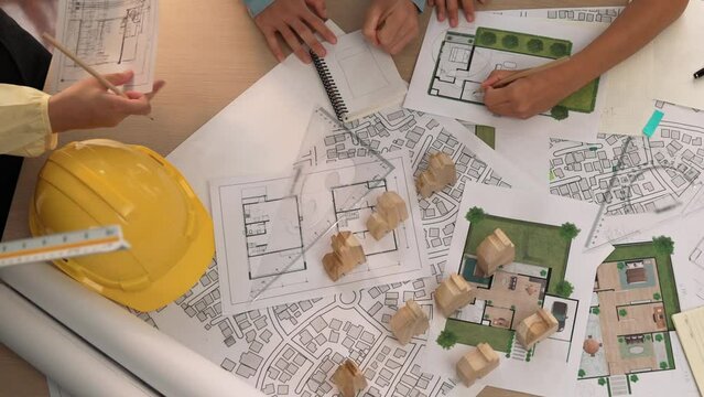 Architect and safety engineer discussion about building construction use blueprint on table with architectural document, measurement tool and wooden block scatter around at modern office. Delineation.