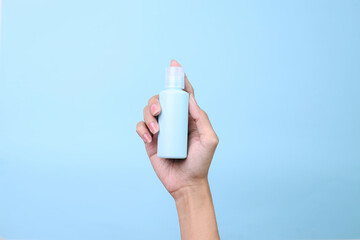 Woman hand holding blank cosmetic spray bottle for mockup isolated over blue background