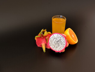 A glass of yellow juice from exotic fruits on a black background, next to pieces of ripe pitaya and orange.