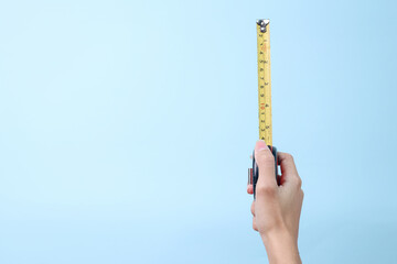 Hand holding a yellow measuring tape over blue background