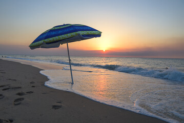 Striped beach umbrella on the beach. Beach umbrella on a sunny day, sea in background. Blue...