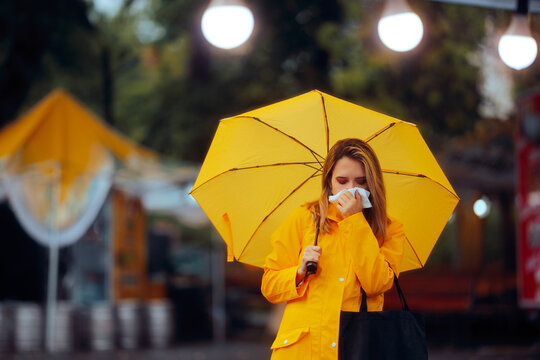 Sick Woman Holding an Umbrella Blowing her Nose. Unwell girl suffering from cold symptoms outdoors 
