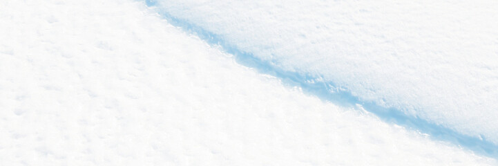 Wide panoramic winter background with snowy ground. Natural snow texture. Wind sculpted patterns on snow surface. Closeup top view with copy space.