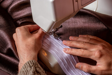 Male hands holding and stitching curtains made of heavy, thick chocolate-colored silk fabric on...