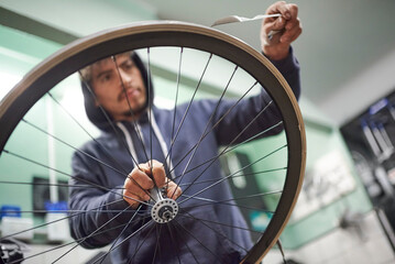 Hispanic man working on a bike painting. Time to remove the masking tape of the wheel rim. Close up...