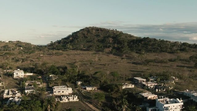 Aerial drone view of small Dominican neighborhood with mountain range at sunset 
