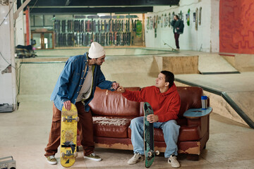 Wide shot of two young gen Z friends greeting each other with fist bump in skatepark, copy space