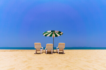 Three Beach Chairs and an umbrella on the sand in summer by the water's edge.