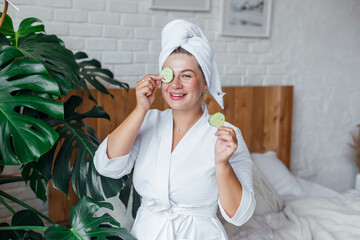 Beautiful women in a white bathrobe after shower making mask with cucumber. Women holding cucumber pads and smile relax with natural homemade