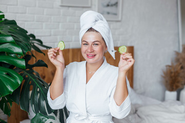 Beautiful women in a white bathrobe after shower making mask with cucumber. Women holding cucumber pads and smile relax with natural homemade