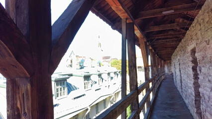 View from a wooden walkway inside a tower, overlooking historic rooftops and a church spire.