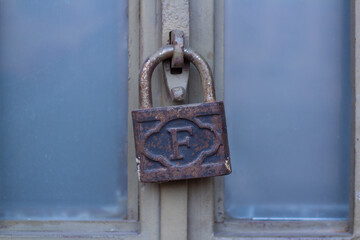 Street photo. Old barn lock with English letter F and pattern hangs on closed blue door close-up....
