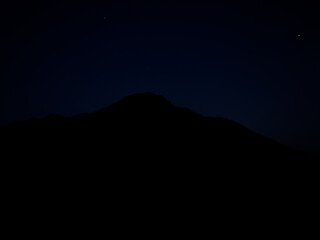 Silhouette of mountain at night with starry sky background.