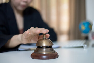  Closeup of a businesswoman hand ringing gold service bell on desk