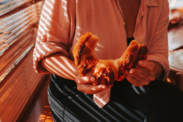 A woman in a pink shirt breaks off a large soft bun with her hands. Fresh, delicious pastries in the morning for breakfast.