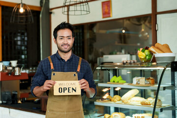 Multiethnic male cafe owner businessman standing smiling and holding signboard saying open in...