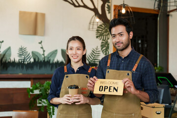 Owner of small cafe, business couple Beautiful Asian woman holding coffee mug standing smiling men of different nationalities. man holding sign saying welcome open. Inside store in front of counter