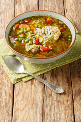 Aguadito de pollo is a traditional Peruvian soup prepared with chicken, aji amarillo peppers, peas, corn, onions, potatoes, rice, and cilantro closeup on the bowl on the wooden table. Vertical