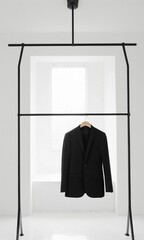Black suit hanging on black hanger in white room with window.