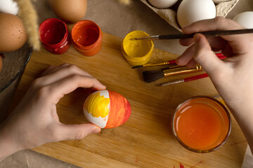 The child takes a white egg and paints it with bright colors