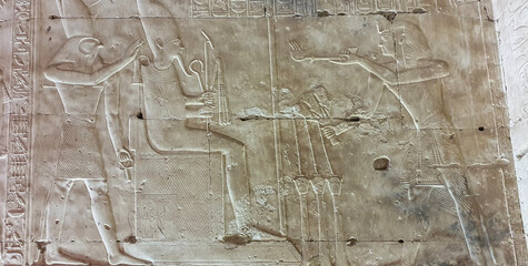 Pharoah Seti I makes offerings to Osiris seated and Horus in a wall relief in the Temple of Seti...