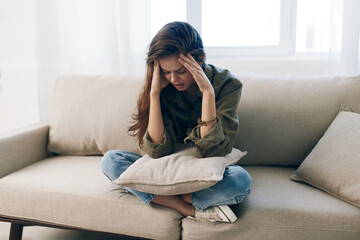 Worried woman sitting on a couch, feeling sad and stressed in her home.