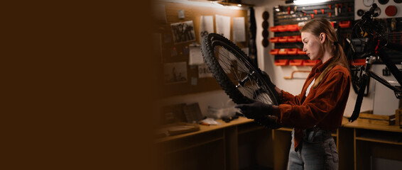 Beautiful young female worker repairing bicycle in her workshop or garage. Bike workshop interior.