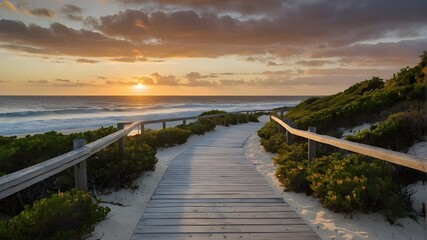 With few bushes throughout its length, the boardwalk leads to a white sand beach and the ocean at sunset. - obrazy, fototapety, plakaty