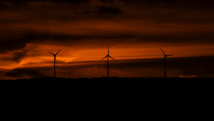 Silhouette of wind turbines at sunset with red sky background.