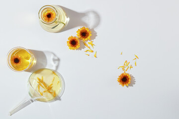 On a white background, laboratory flask decorated with fresh calendula flowers. Minimal background...