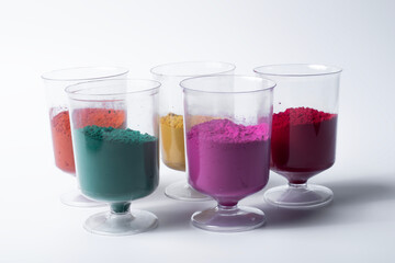 Multicolored holi powder in glass cups on white background.