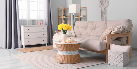 Stylish living room with sofa, chest of drawers, coffee table and bouquet of narcissus flowers