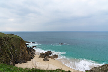 Vue depuis les falaises du littoral breton, le paysage enchanteur se dévoile : plages de sable, gros rochers et eaux turquoises sous un ciel couvert, offrant une perspective époustouflante sur la natu