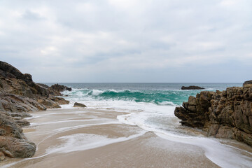 Sur le littoral breton, de majestueux rochers parsèment la plage, offrant un spectacle époustouflant : sable, falaises et eaux turquoises sous un ciel couvert, une invitation à l'émerveillement
