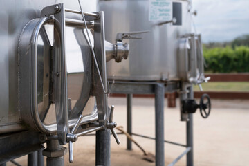 Stainless steel vats for fermentation in a wine factory. Steel barrels in winery outdoors, vines in background