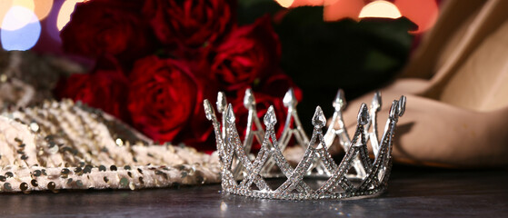 Crown with heels, roses and prom dress on table against blurred lights, closeup