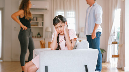 Annoyed and unhappy young girl sitting on sofa trapped in middle of tension by her parent argument...