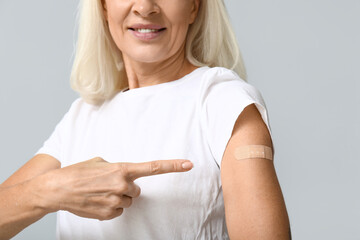 Mature woman with medical patch on arm against grey background. Vaccination concept